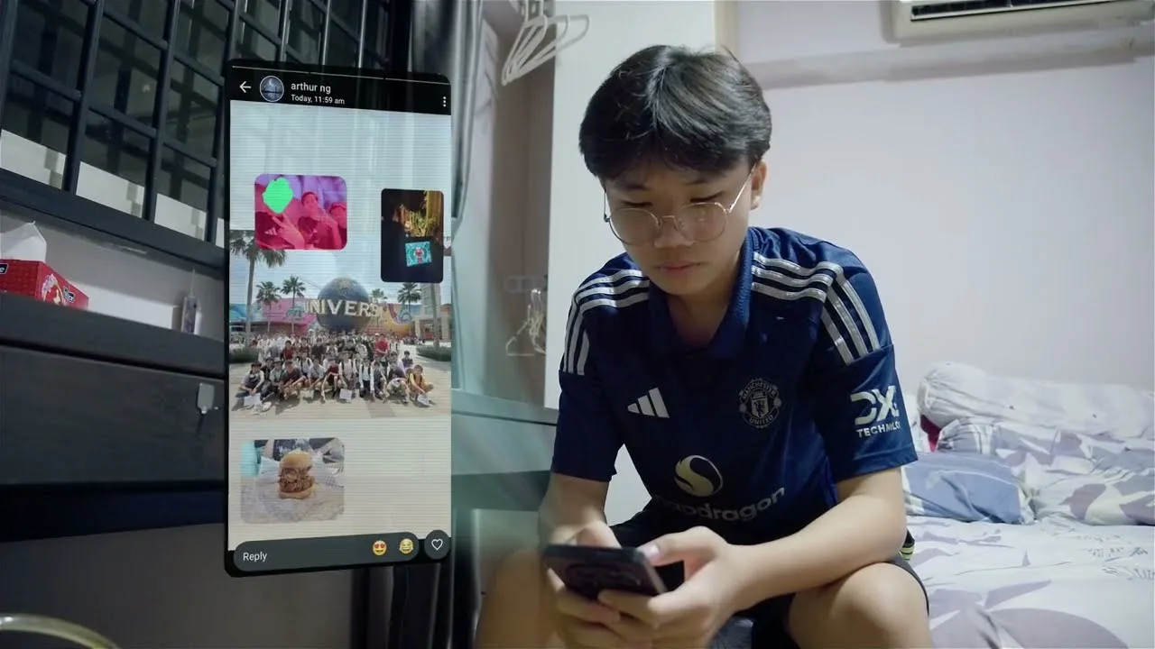 A boy in a football jersey scrolls through group photos on his phone in his bedroom