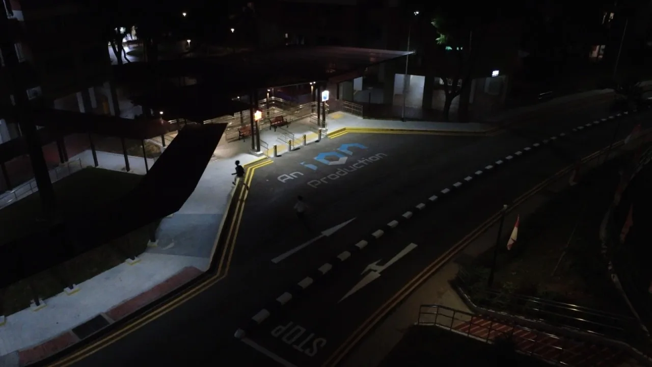 An empty road at night outside an HDB block, with the production title painted on the tarmac